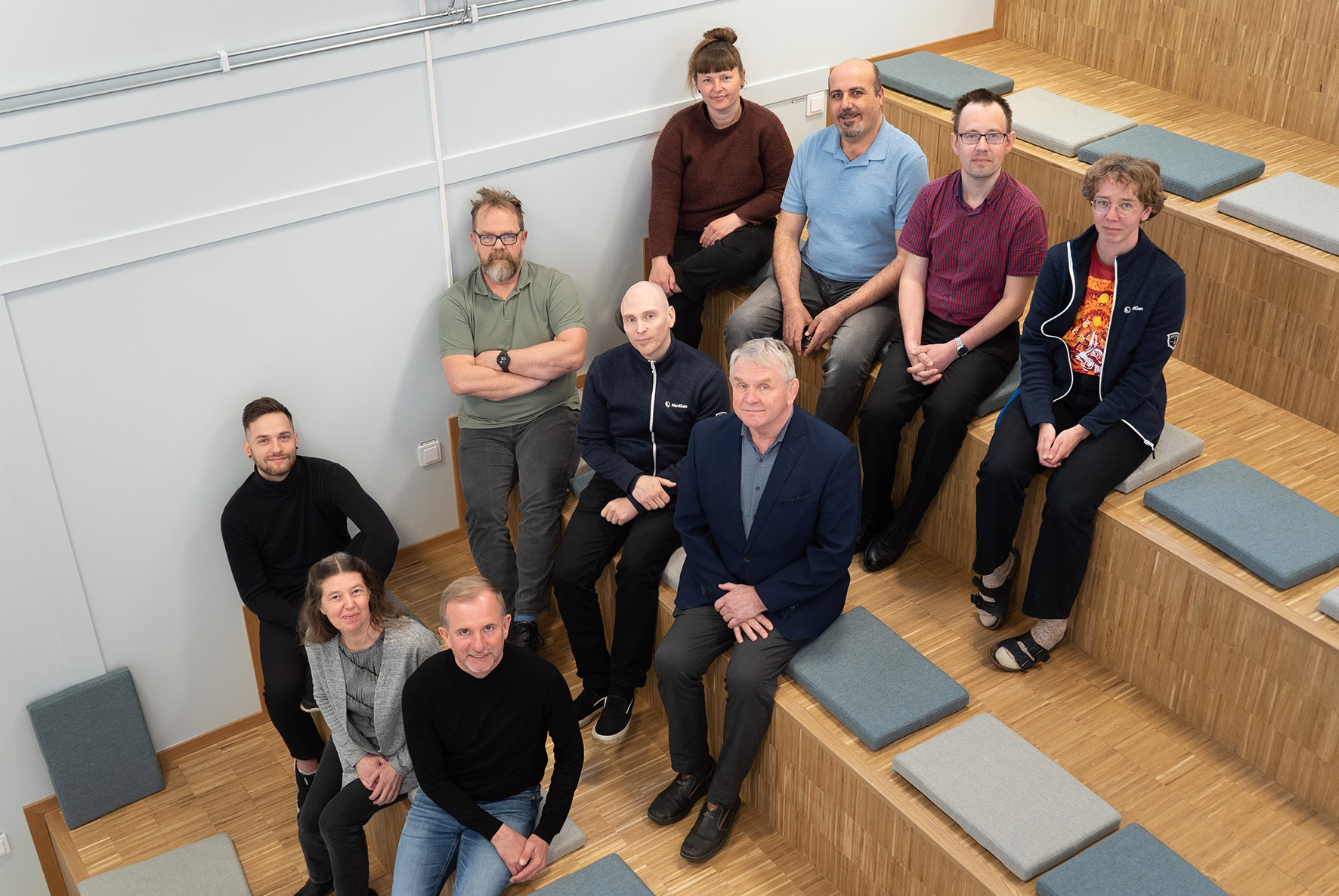 Group photo of ten persons sitting in something that looks like a very large stair. 