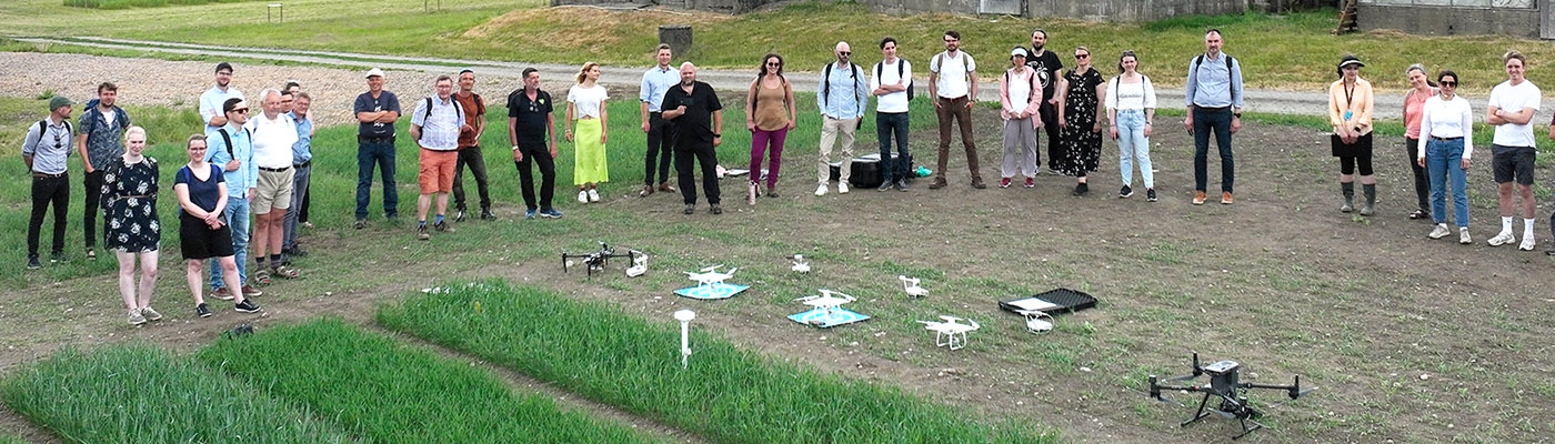 A group of people standing in front of different drones placed nearby a green field. 