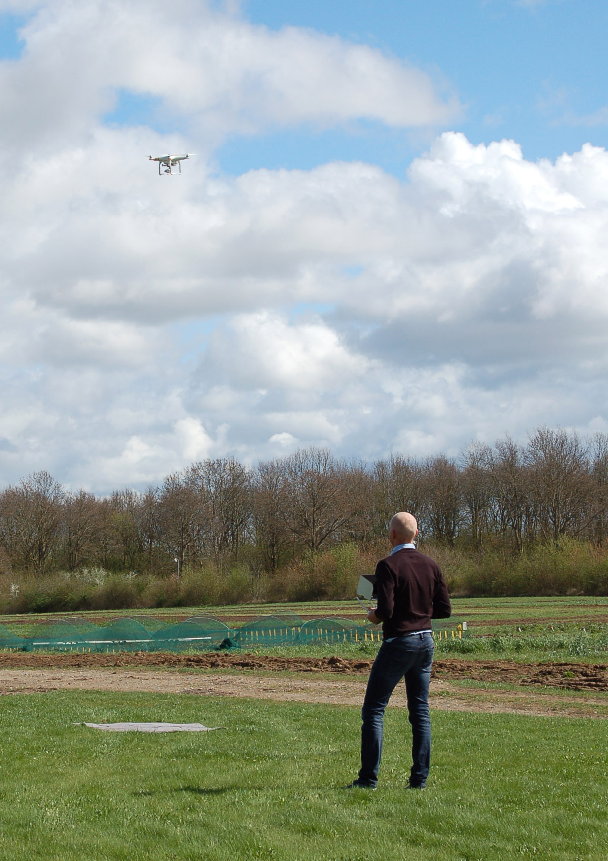 A man stands on the ground looking at a flying drone. 